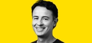 Fundo amarelo, foto em branco e preto. Homem entre 30 e 40 anos, de cabelo curto, sorrindo. 