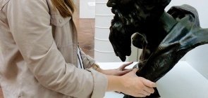 Jovem loira, usa um fone de ouvido preto, ela toca uma escultura