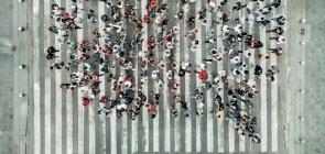 Grupo de pessoas paradas em pé, em cima de uma faixa de pedestres, usando roupas coloridas e vistas de cima, formando a imagem de um balão de fala de histórias em quadrinhos
