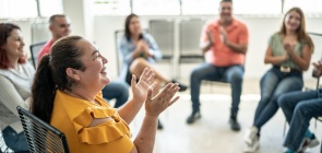 Grupo de professores, sentados em roda, sorriem e batem palma