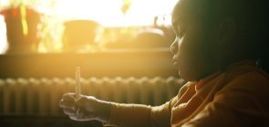 Aluna escrevendo sentada em uma carteira, de perfil, com o sol brilhando